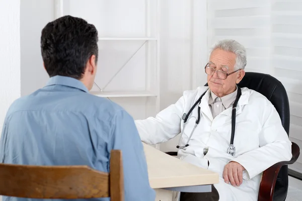 Male patient having consultation with old Doctor in consulting r Stock Photo
