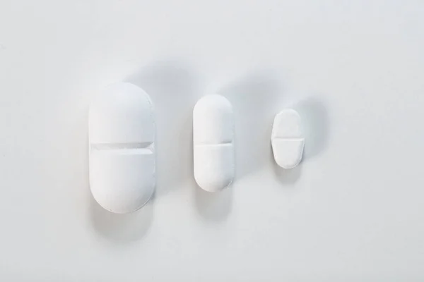 上から3枚の異なるサイズの錠剤を白で見る — ストック写真