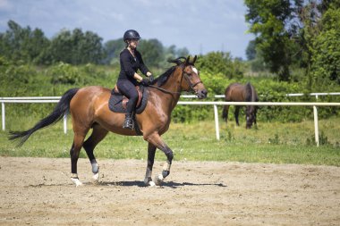 Siyahlı kız binicilik okulunda ata biniyor.