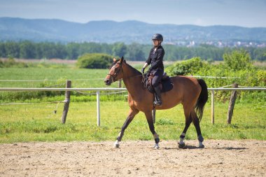 Siyahlı kız binicilik okulunda ata biniyor.