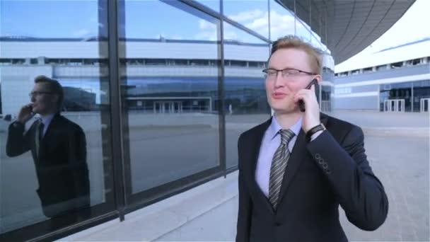 Joven hombre de negocios está caminando y hablando por teléfono (steadicam disparo ) — Vídeo de stock