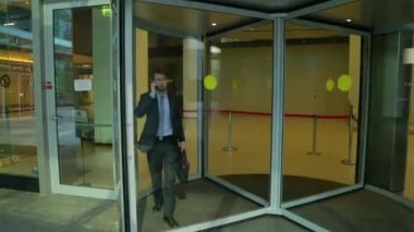 Yakışıklı adam acele (steadicam shot telefonda konuşurken iş merkezinin dışında cam döner kapılar geliyor)