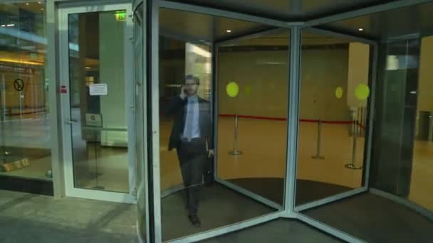 Un bell'uomo sta uscendo dalle porte girevoli di vetro del business center, parlando al telefono (tiro steadicam ) — Video Stock