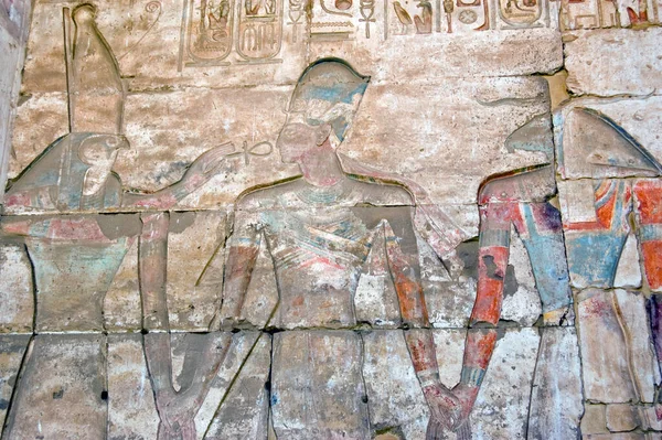 Ancient Egyptian hieroglyphic, painted carving showing the falcon headed god Horus and the goat headed creator god Khnum with the Pharoah Ramses II between them. Outer wall of the Temple to Osiris at Abydos, Egypt.