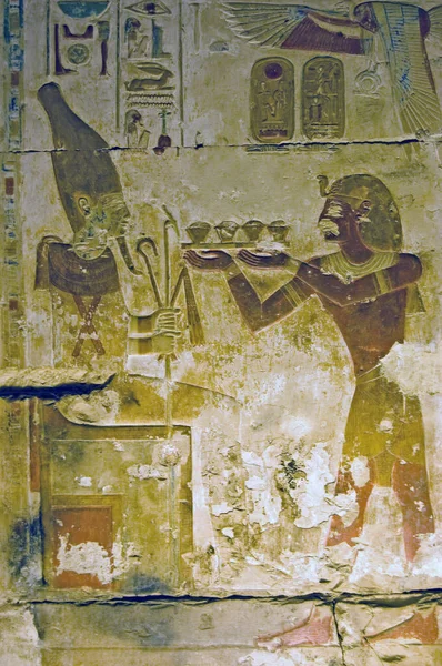 Ancient egyptian hieroglyphic painted carving showing the Pharoah Seti making an offering to the god of regeneration Osiris. Temple of Osiris, Abydos, Egypt. The tray of food being proffered looks suspiciously like cupcakes.