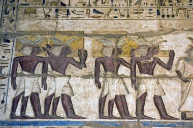 A painted and carved hieroglyphic illustration on a wall at Medinet Habu temple on the West Bank of the Nile at Luxor. Showing priests carrying golden offerings into the temple. Carving is thousands of years old. clipart
