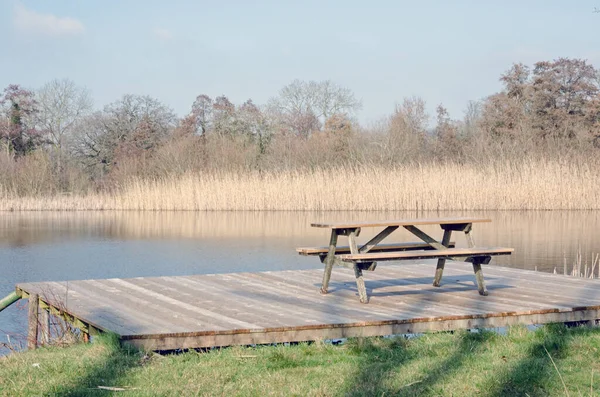 Peaceful scene of a picnic table overlooking a lake in Berkshire, England on a sunny spring day.