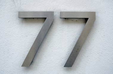 Londra 'da bir binanın dışındaki kaba, beyaz boyalı bir duvarda 77 numara için fırçalanmış metal figürler..