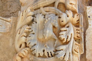 Libya 'nın kuzey kıyısındaki tarihi Leptis Magna harabelerinde Severan Kemeri' nde bitki dallarıyla çevrili bir atın antik Roma levrek kabartması..