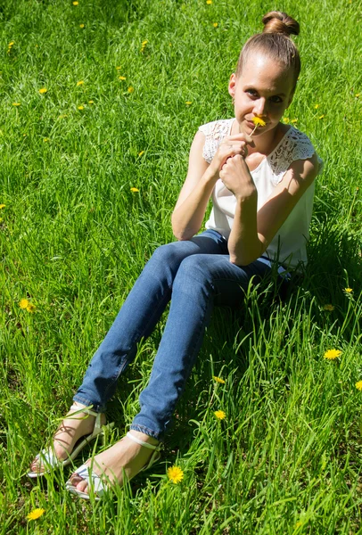 Chica sentada en la hierba con diente de león en la mano — Foto de Stock