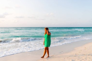 Kız sahilde elbiseyle yürüyor.