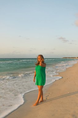 Kız sahilde elbiseyle yürüyor.