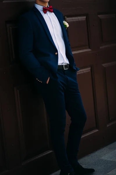 Novio vestido con traje azul y corbata en la puerta roja . — Foto de Stock