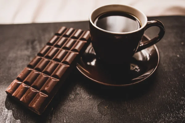 Cup of coffee with grains and chocolate on wooden table on dark background — Stock Photo, Image