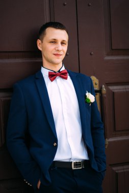  Mavi takım elbise ve papyon kırmızı kapıda giyen damat. 