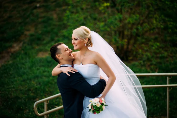 Bruidegom bezit een bruid op bruiloft dag buitenshuis knuffelen op lente nb — Stockfoto
