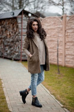 Bahar country tarzında. Beyaz örgü kazak ve kürklü şapka ayakta house, giyen kazak rahat yakınındaki bahçedeki rustik ahşap duvar önünde genç kadın portresi tam uzunlukta.