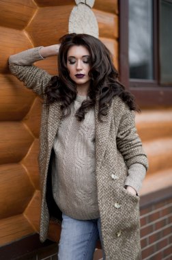 Bahar country tarzında. Beyaz örgü kazak ve kürklü şapka ayakta house, giyen kazak rahat yakınındaki bahçedeki rustik ahşap duvar önünde genç kadın portresi tam uzunlukta.