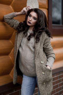 Bahar country tarzında. Beyaz örgü kazak ve kürklü şapka ayakta house, giyen kazak rahat yakınındaki bahçedeki rustik ahşap duvar önünde genç kadın portresi tam uzunlukta.