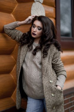 Bahar country tarzında. Beyaz örgü kazak ve kürklü şapka ayakta house, giyen kazak rahat yakınındaki bahçedeki rustik ahşap duvar önünde genç kadın portresi tam uzunlukta.