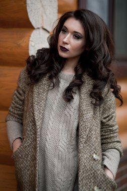 Bahar country tarzında. Beyaz örgü kazak ve kürklü şapka ayakta house, giyen kazak rahat yakınındaki bahçedeki rustik ahşap duvar önünde genç kadın portresi tam uzunlukta.