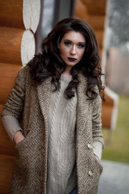 Bahar country tarzında. Beyaz örgü kazak ve kürklü şapka ayakta house, giyen kazak rahat yakınındaki bahçedeki rustik ahşap duvar önünde genç kadın portresi tam uzunlukta.