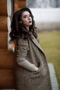 Bahar country tarzında. Beyaz örgü kazak ve kürklü şapka ayakta house, giyen kazak rahat yakınındaki bahçedeki rustik ahşap duvar önünde genç kadın portresi tam uzunlukta.