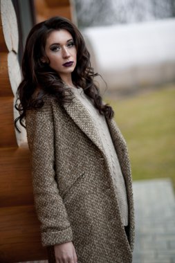 Bahar country tarzında. Beyaz örgü kazak ve kürklü şapka ayakta house, giyen kazak rahat yakınındaki bahçedeki rustik ahşap duvar önünde genç kadın portresi tam uzunlukta.