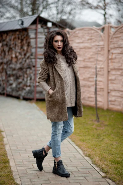 Bahar country tarzında. Beyaz örgü kazak ve kürklü şapka ayakta house, giyen kazak rahat yakınındaki bahçedeki rustik ahşap duvar önünde genç kadın portresi tam uzunlukta.