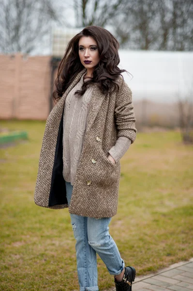 Spring in the country style. Full length portrait of young woman in white knitted sweater and furry hat standing in the front of rustic wood wall in the yard near house, wearing sweater casual. — Stock Photo, Image