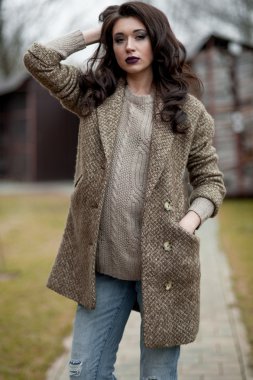 Bahar country tarzında. Beyaz örgü kazak ve kürklü şapka ayakta house, giyen kazak rahat yakınındaki bahçedeki rustik ahşap duvar önünde genç kadın portresi tam uzunlukta.