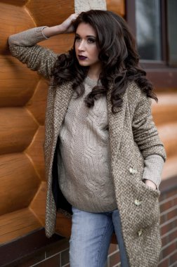 Bahar country tarzında. Beyaz örgü kazak ve kürklü şapka ayakta house, giyen kazak rahat yakınındaki bahçedeki rustik ahşap duvar önünde genç kadın portresi tam uzunlukta.