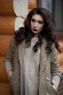 Bahar country tarzında. Beyaz örgü kazak ve kürklü şapka ayakta house, giyen kazak rahat yakınındaki bahçedeki rustik ahşap duvar önünde genç kadın portresi tam uzunlukta.