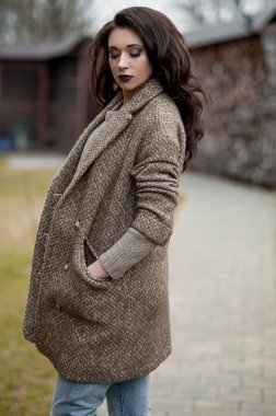 Bahar country tarzında. Beyaz örgü kazak ve kürklü şapka ayakta house, giyen kazak rahat yakınındaki bahçedeki rustik ahşap duvar önünde genç kadın portresi tam uzunlukta.