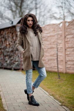 Bahar country tarzında. Beyaz örgü kazak ve kürklü şapka ayakta house, giyen kazak rahat yakınındaki bahçedeki rustik ahşap duvar önünde genç kadın portresi tam uzunlukta.