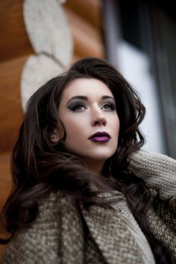 Bahar country tarzında. Beyaz örgü kazak ve kürklü şapka ayakta house, giyen kazak rahat yakınındaki bahçedeki rustik ahşap duvar önünde genç kadın portresi tam uzunlukta.