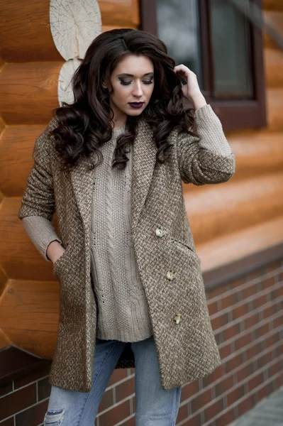 Bahar country tarzında. Beyaz örgü kazak ve kürklü şapka ayakta house, giyen kazak rahat yakınındaki bahçedeki rustik ahşap duvar önünde genç kadın portresi tam uzunlukta.