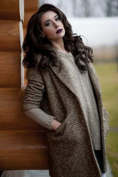 Bahar country tarzında. Beyaz örgü kazak ve kürklü şapka ayakta house, giyen kazak rahat yakınındaki bahçedeki rustik ahşap duvar önünde genç kadın portresi tam uzunlukta.