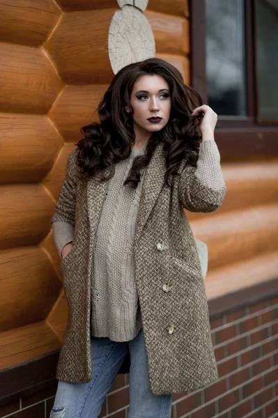 Bahar country tarzında. Beyaz örgü kazak ve kürklü şapka ayakta house, giyen kazak rahat yakınındaki bahçedeki rustik ahşap duvar önünde genç kadın portresi tam uzunlukta.