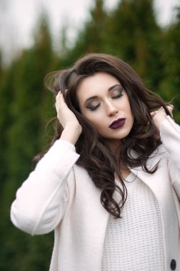 Beautiful fashionable woman in a black hat and white coat posing outdoors