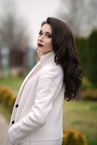 Mulher elegante bonita em um chapéu preto e casaco branco posando ao ar livre — Fotografia de Stock