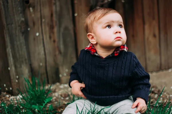 Piękne dziecko chłopiec siedzi na zielonej trawie, 9 w tle drewna — Zdjęcie stockowe