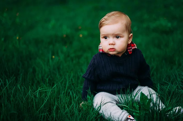 Piękny chłopiec siedzący wśród zielona trawa trawnik wiosna — Zdjęcie stockowe