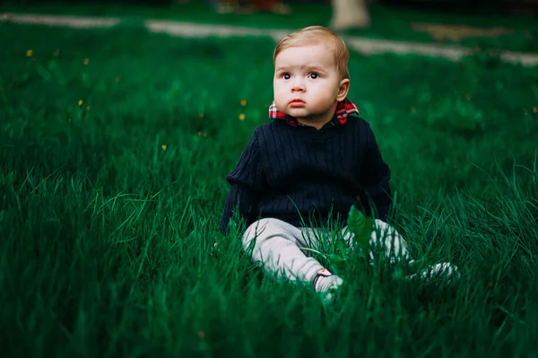 Krásný chlapeček sedí mezi zelené trávě na jaře trávníku — Stock fotografie