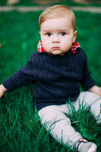beautiful baby boy sitting among green grass on spring lawn