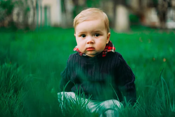 Menino bonito sentado entre grama verde no gramado da primavera — Fotografia de Stock