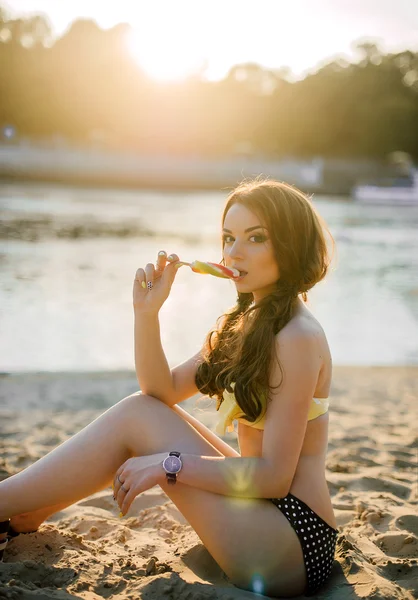 暑假期间，旅游、 观光、 垃圾食品与人们观念-太阳镜在度假村海滩背景，穿着黄色的泳衣上吃多彩的冰激淋的年轻女子 — 图库照片