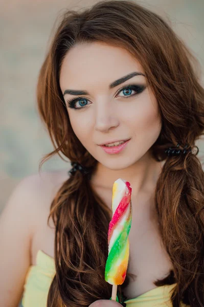 Summer vacation, travel, tourism, junk food and people concept - young woman in sunglasses eating colorful ice cream on resort beach background, wearing yellow swimsuit — Stock Photo, Image