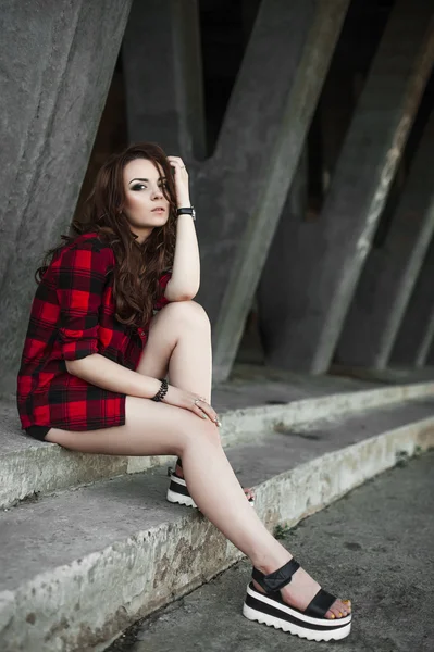 Menina bonita hipster posando e sorrindo perto de fundo da parede urbana em camisa xadrez vermelho, shorts, ao ar livre retrato de verão . — Fotografia de Stock