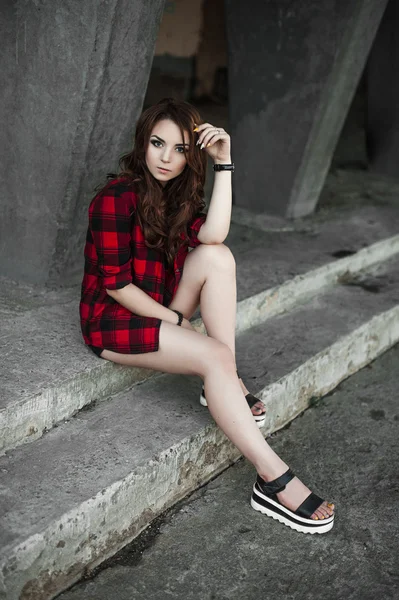 Menina bonita hipster posando e sorrindo perto de fundo da parede urbana em camisa xadrez vermelho, shorts, ao ar livre retrato de verão . — Fotografia de Stock